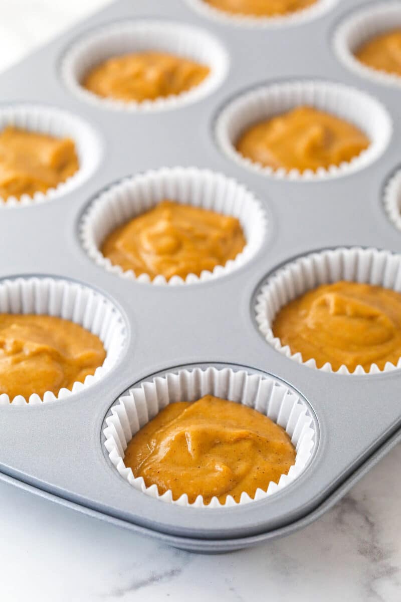 Cupcake liners filled 3/4 with pumpkin batter in a cupcake pan.