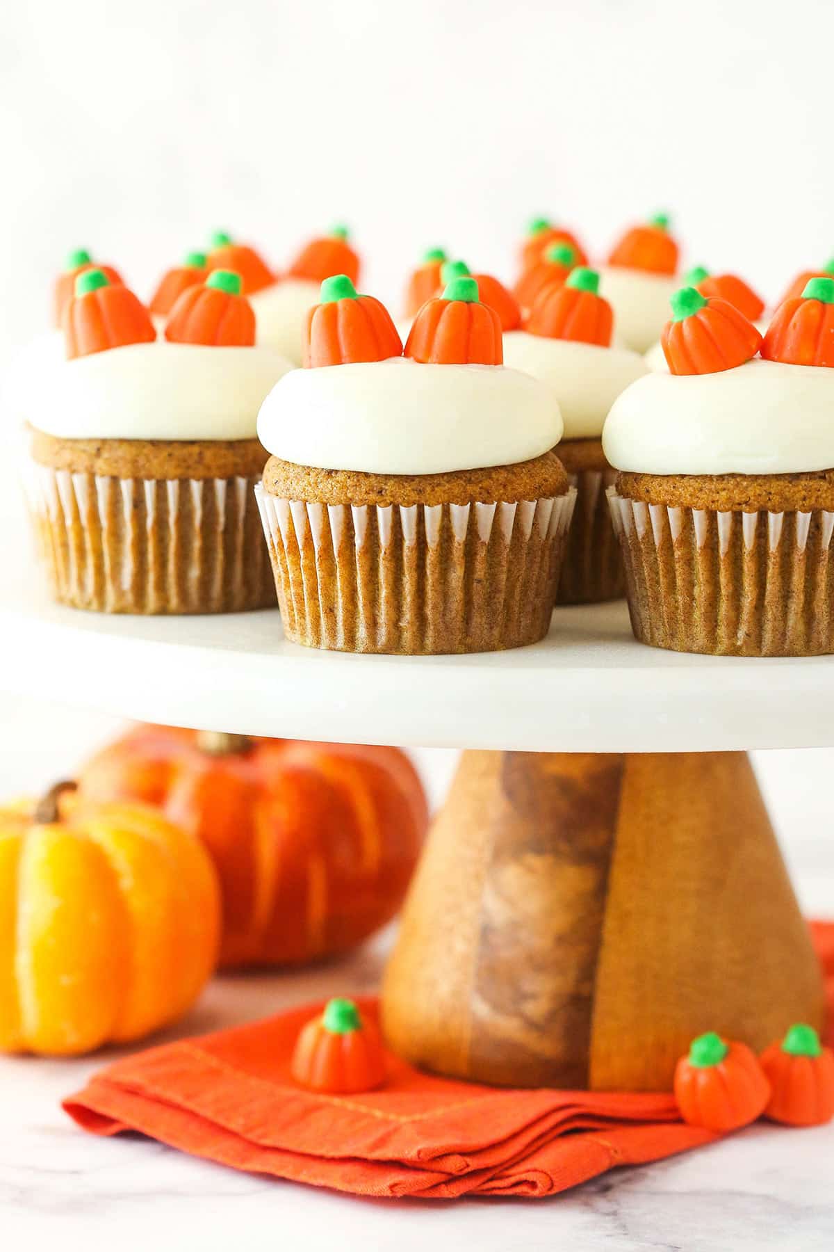 Pumpkin cupcakes on a cake stand near small pumpkins and pumpkin candies.