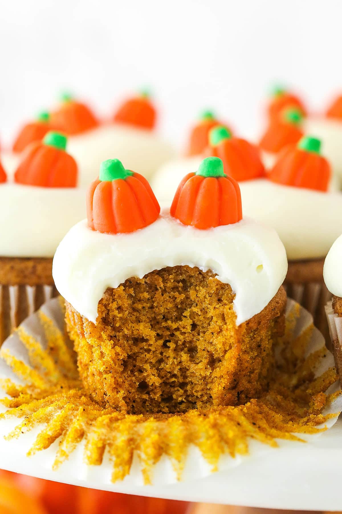 These moist pumpkin cupcakes are topped with a big dollop of melt-in-your-mouth cream cheese frosting! Meet your new favorite fall dessert. A pumpkin cupcake with a bite taken out of it.