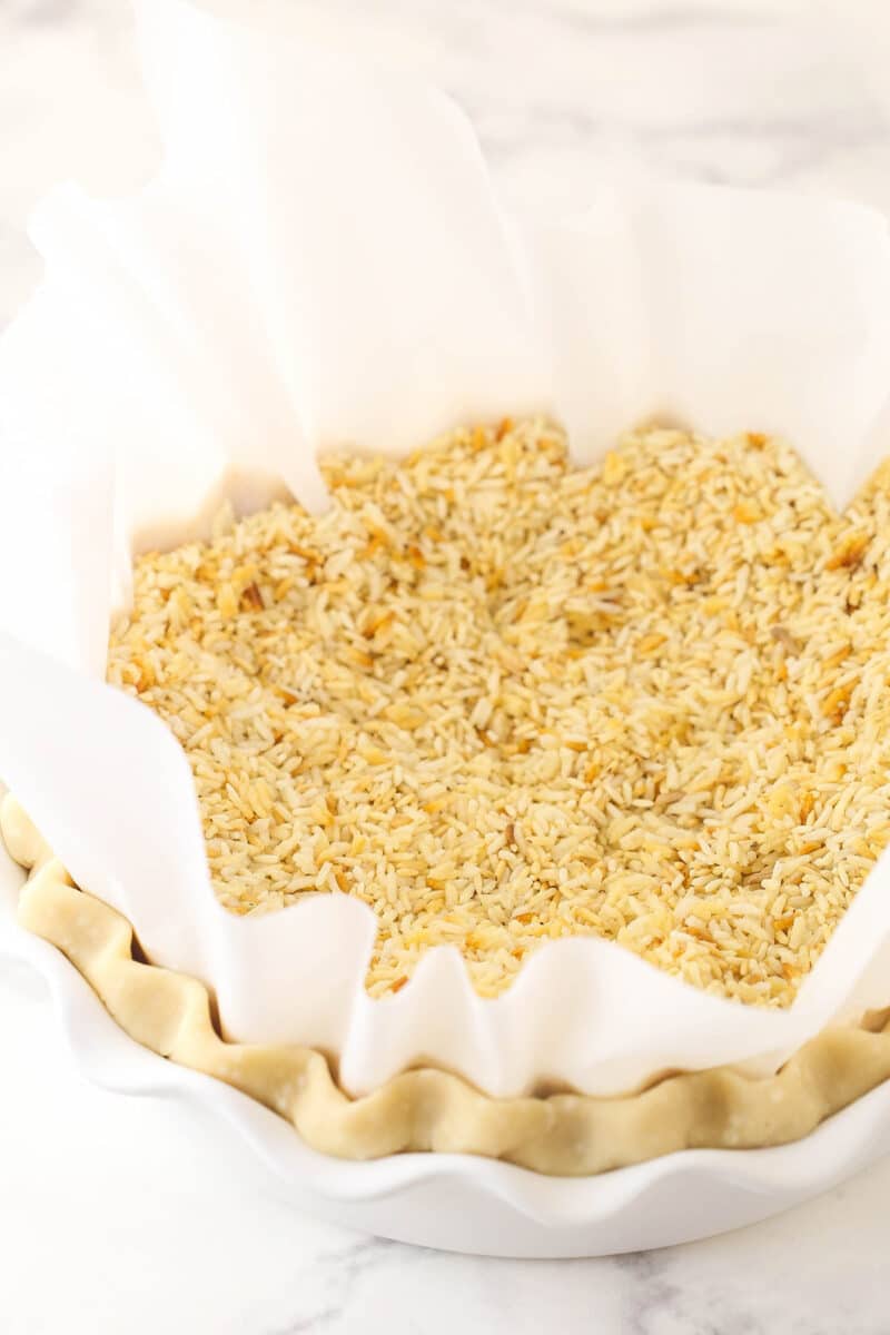 Covering a refrigerated pie crust with parchment paper and filling it with dry rice to blind bake.