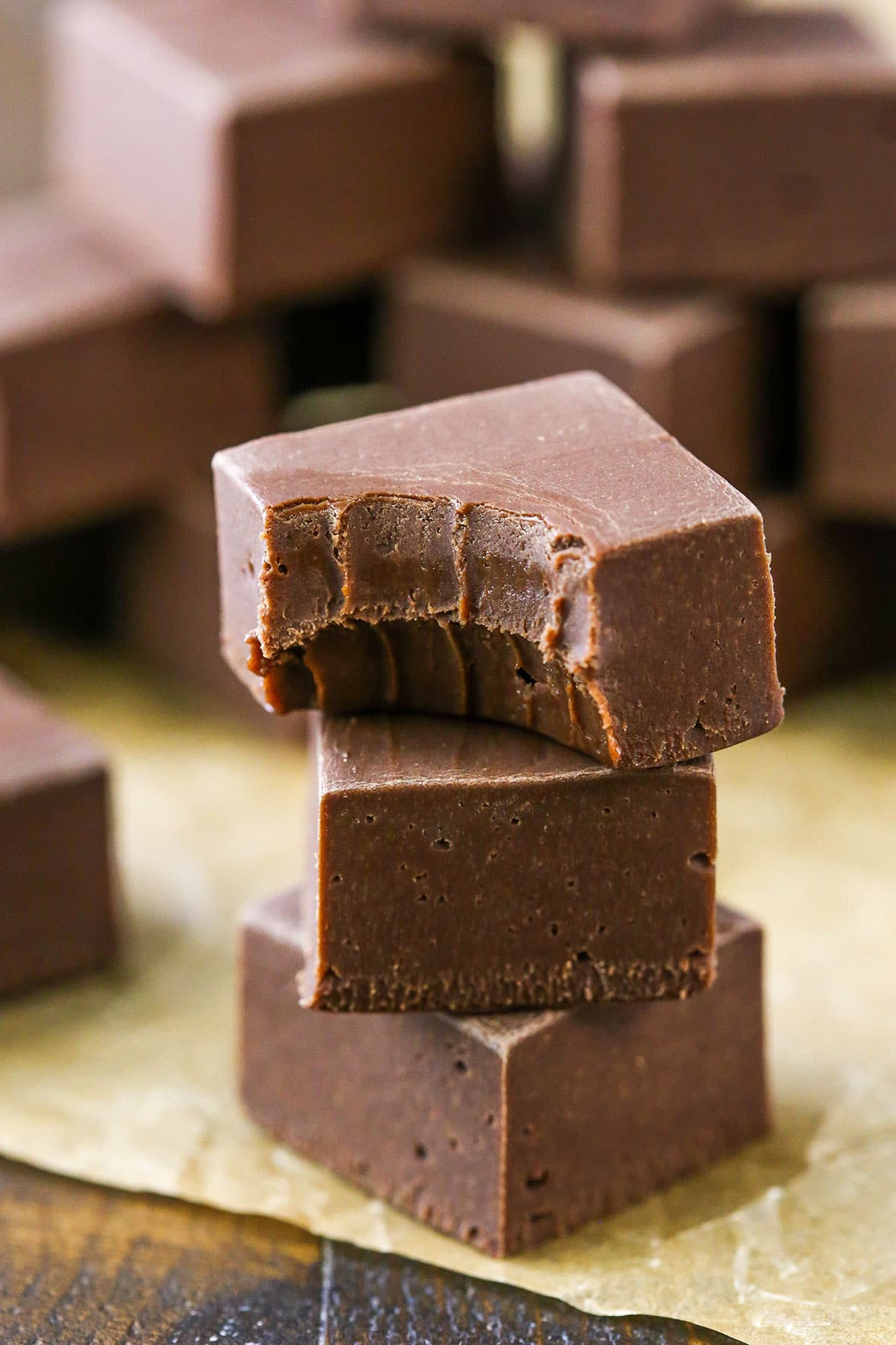This Easy Chocolate Fudge recipe is made with just 3 ingredients! Chocolate chips, sweetened condensed milk and vanilla come together to make a homemade fudge that's bursting with chocolate flavor. It's a simple treat to put together for gifts and sharing this holiday season. Quick and Easy Chocolate Fudge cubes stacked on a table
