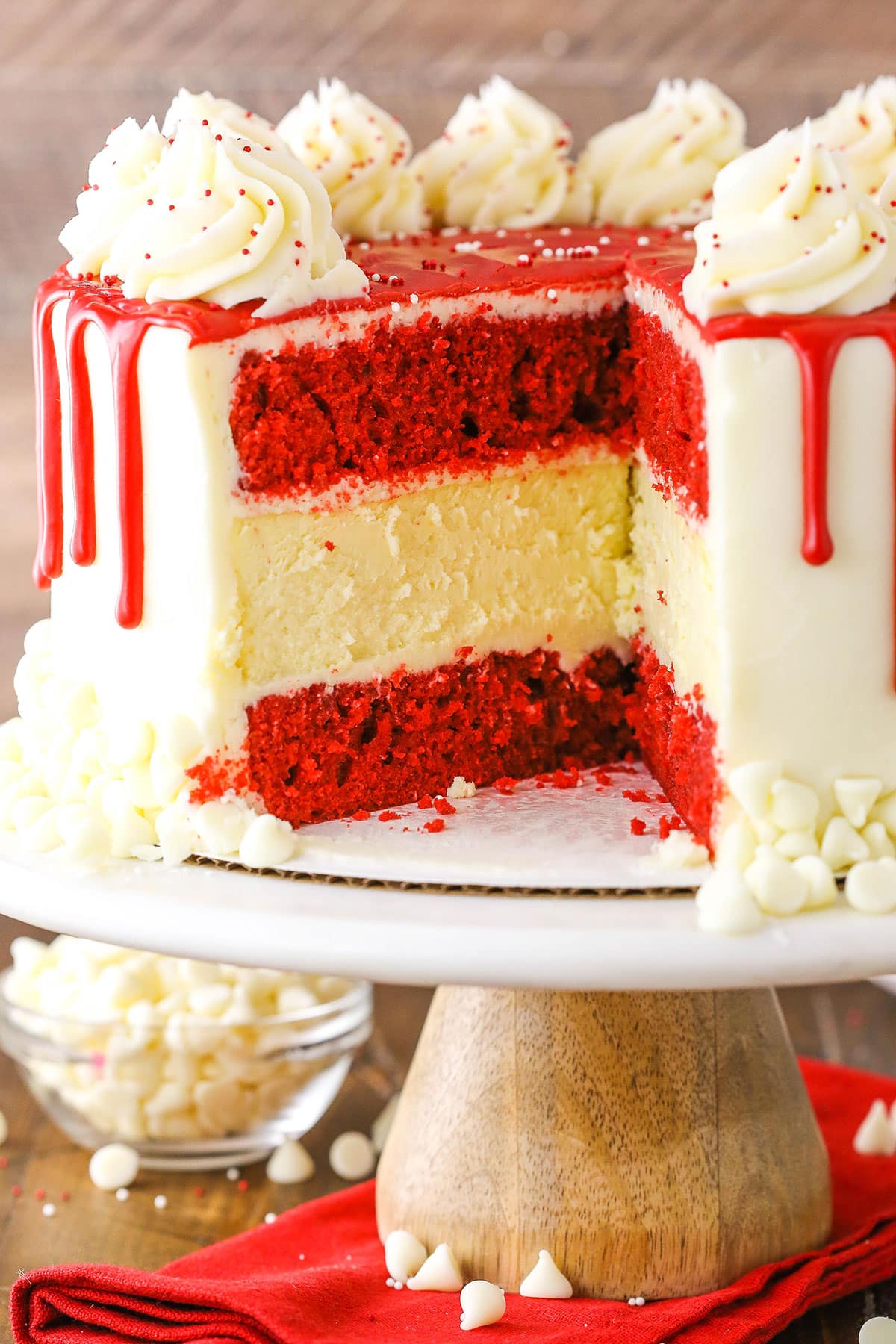 Side view of a Red Velvet Cheesecake Cake with a slice removed on a wooden cake stand