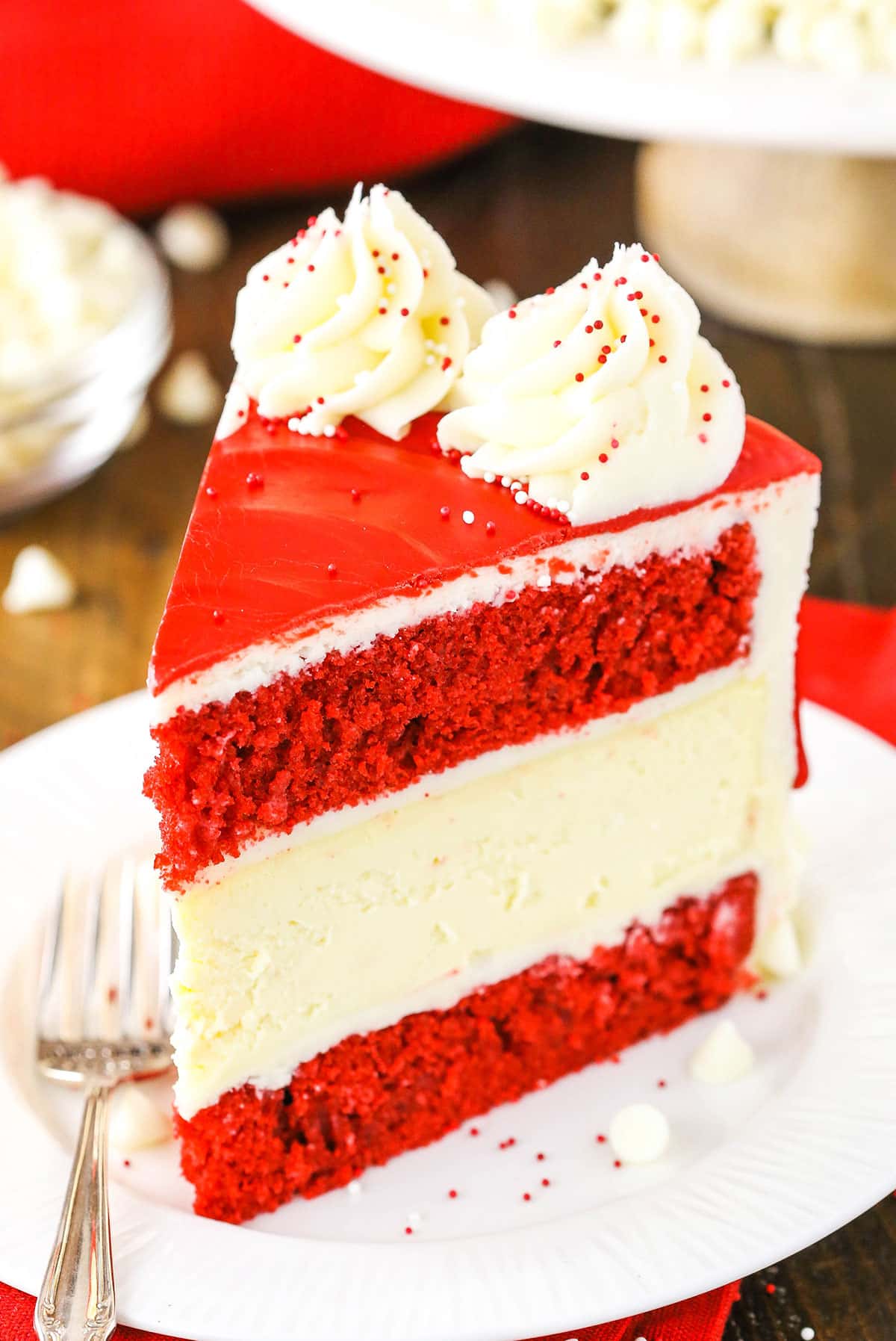 A slice of Red Velvet Cheesecake Cake next to a silver fork on a white plate