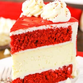 A slice of Red Velvet Cheesecake Cake next to a silver fork on a white plate