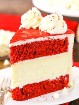 A slice of Red Velvet Cheesecake Cake next to a silver fork on a white plate