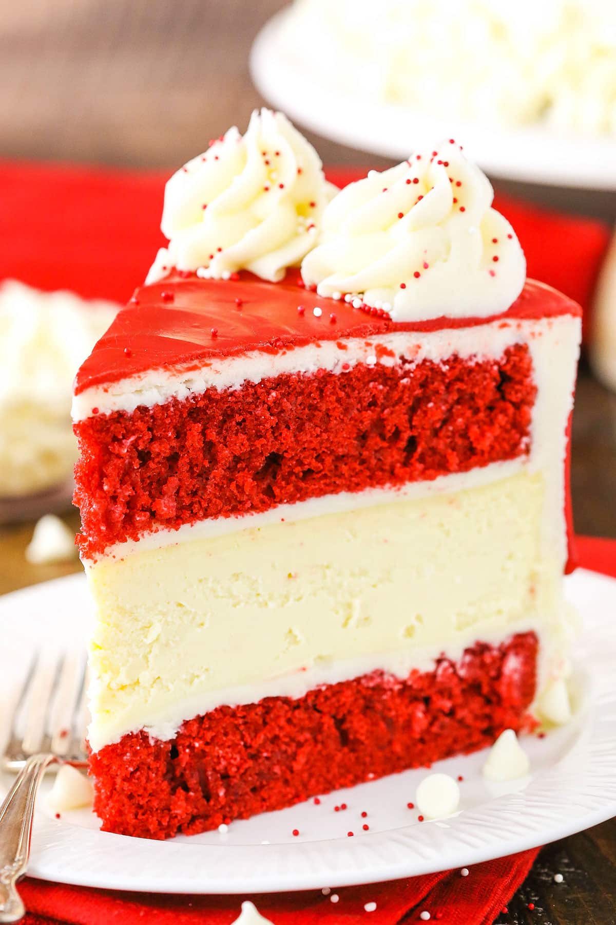 A slice of Red Velvet Cheesecake Cake next to a silver fork on a white plate