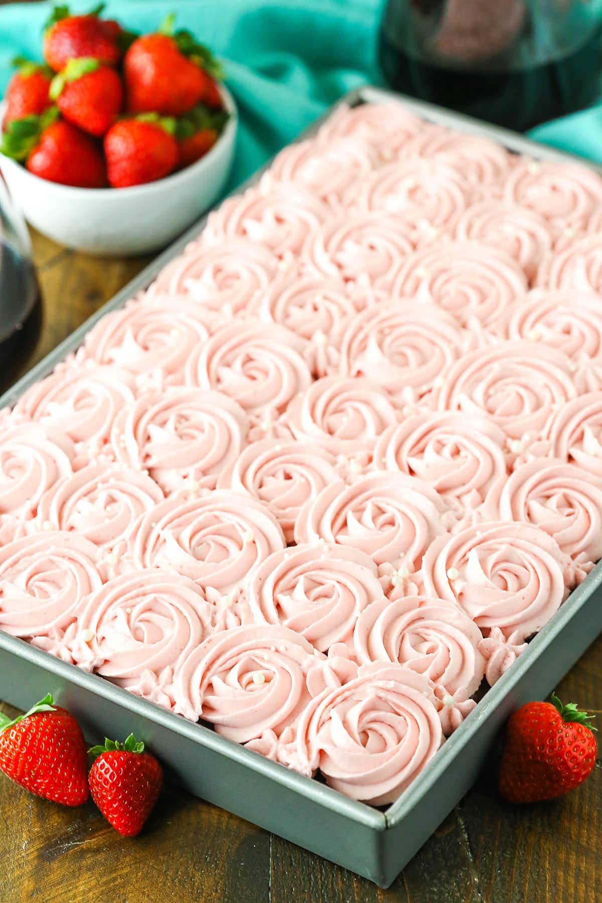 Red Wine Chocolate Poke Cake is a moist chocolate cake made with red wine, then soaked with more chocolate and red wine! Overhead view of a full Red Wine Chocolate Poke Cake in a metal cake pan with strawberries in the background