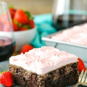 A square slice of Red Wine Chocolate Poke Cake next to a fork on a gray plate