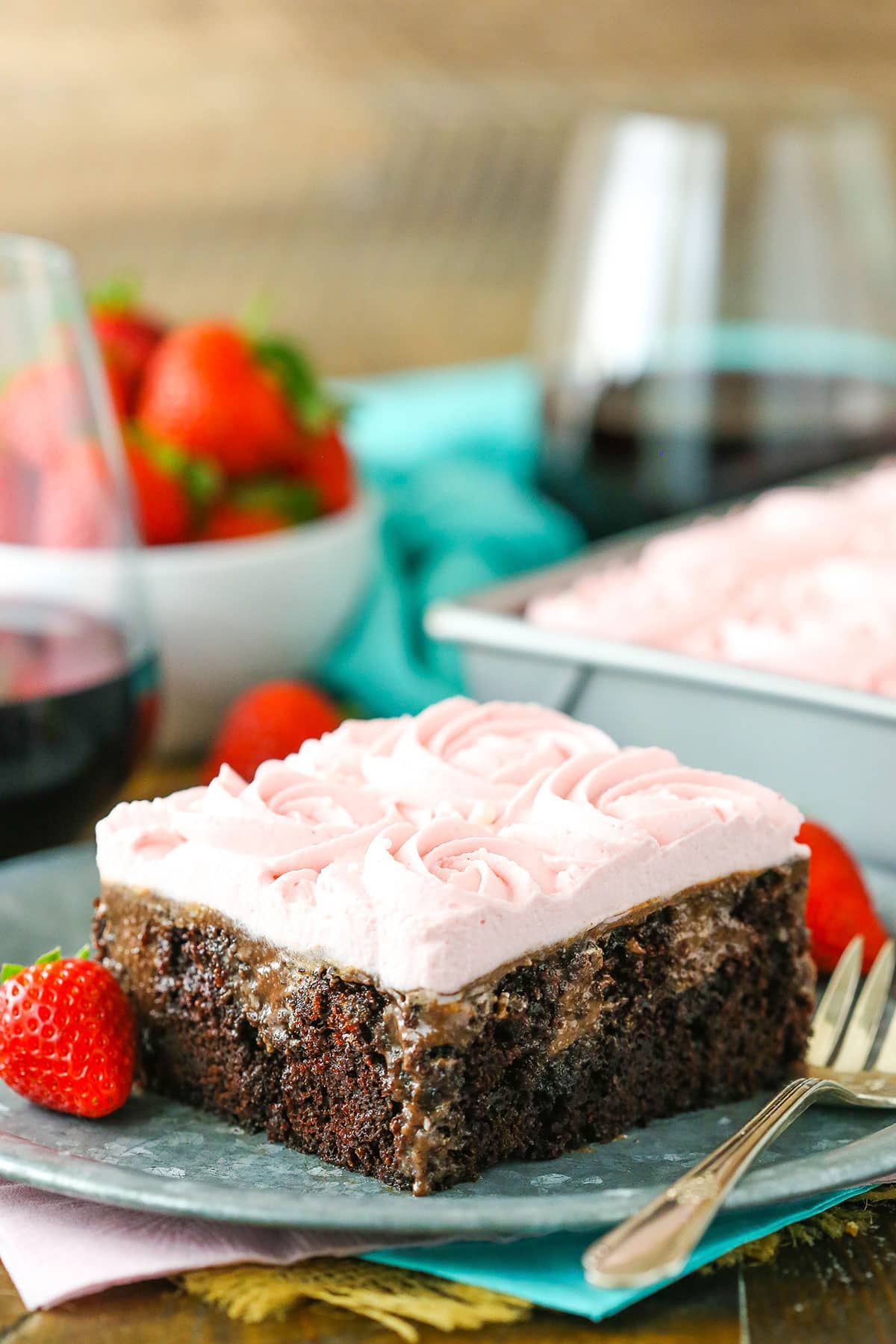 A square slice of Red Wine Chocolate Poke Cake next to a fork on a gray plate