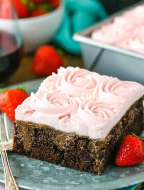 A square slice of Red Wine Chocolate Poke Cake with a bite removed next to a fork on a gray plate