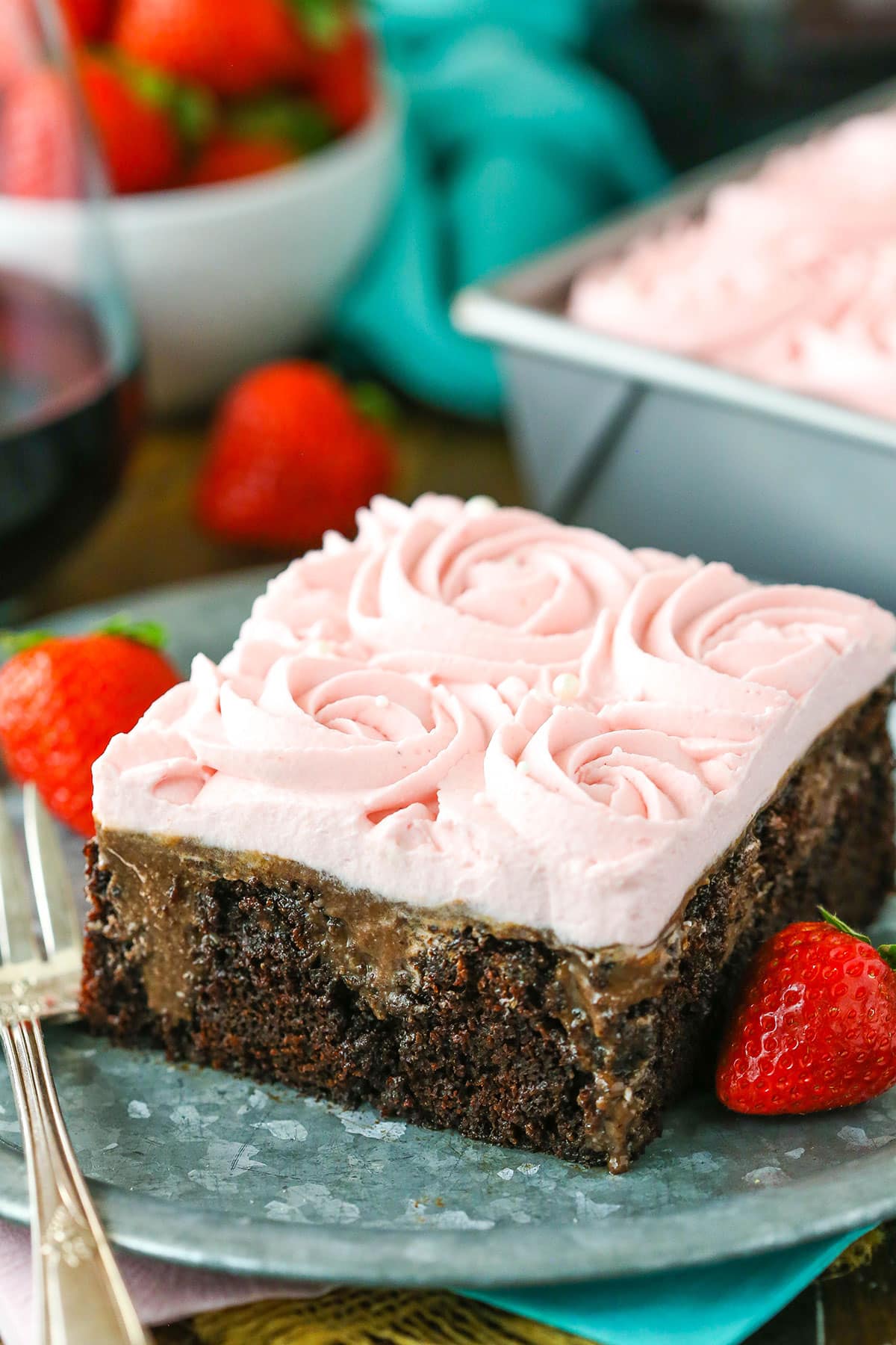 A square slice of Red Wine Chocolate Poke Cake with a bite removed next to a fork on a gray plate