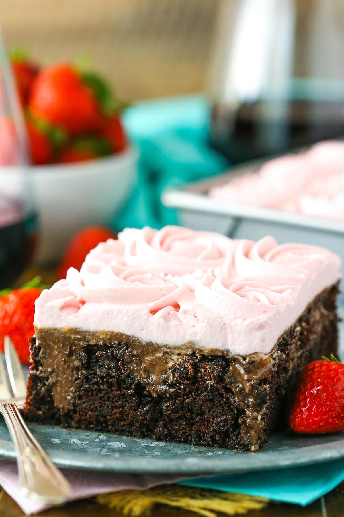 A square slice of Red Wine Chocolate Poke Cake with a bite removed next to a fork on a gray plate