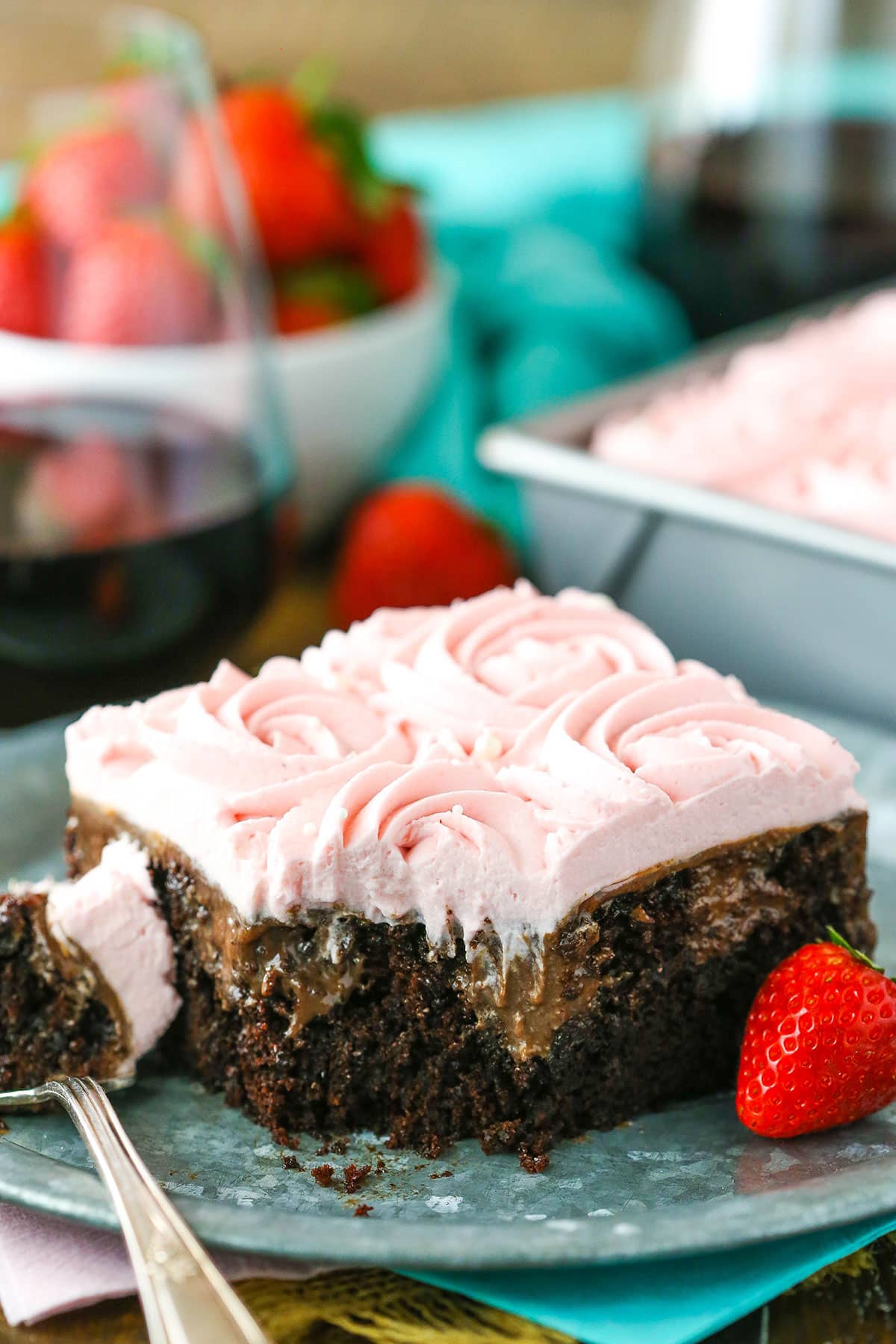 A square slice of Red Wine Chocolate Poke Cake with a bite removed next to a fork on a gray plate