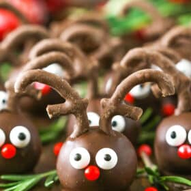 Side view of Reindeer Cookie Balls on a wooden table surrounded by rosemary