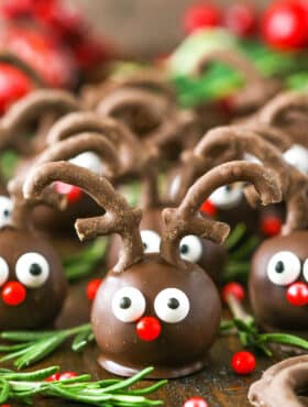 Side view of Reindeer Cookie Balls on a wooden table surrounded by rosemary