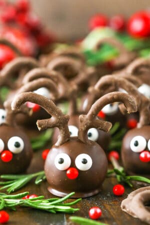 Side view of Reindeer Cookie Balls on a wooden table surrounded by rosemary