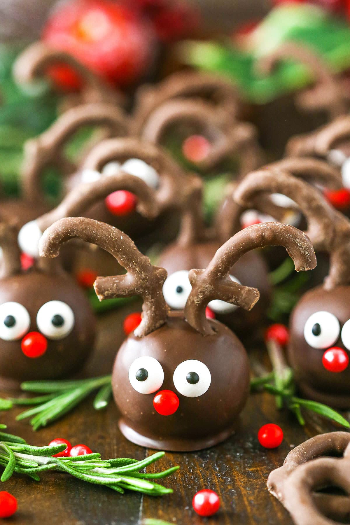 Side view of Reindeer Cookie Balls on a wooden table and surrounded by rosemary
