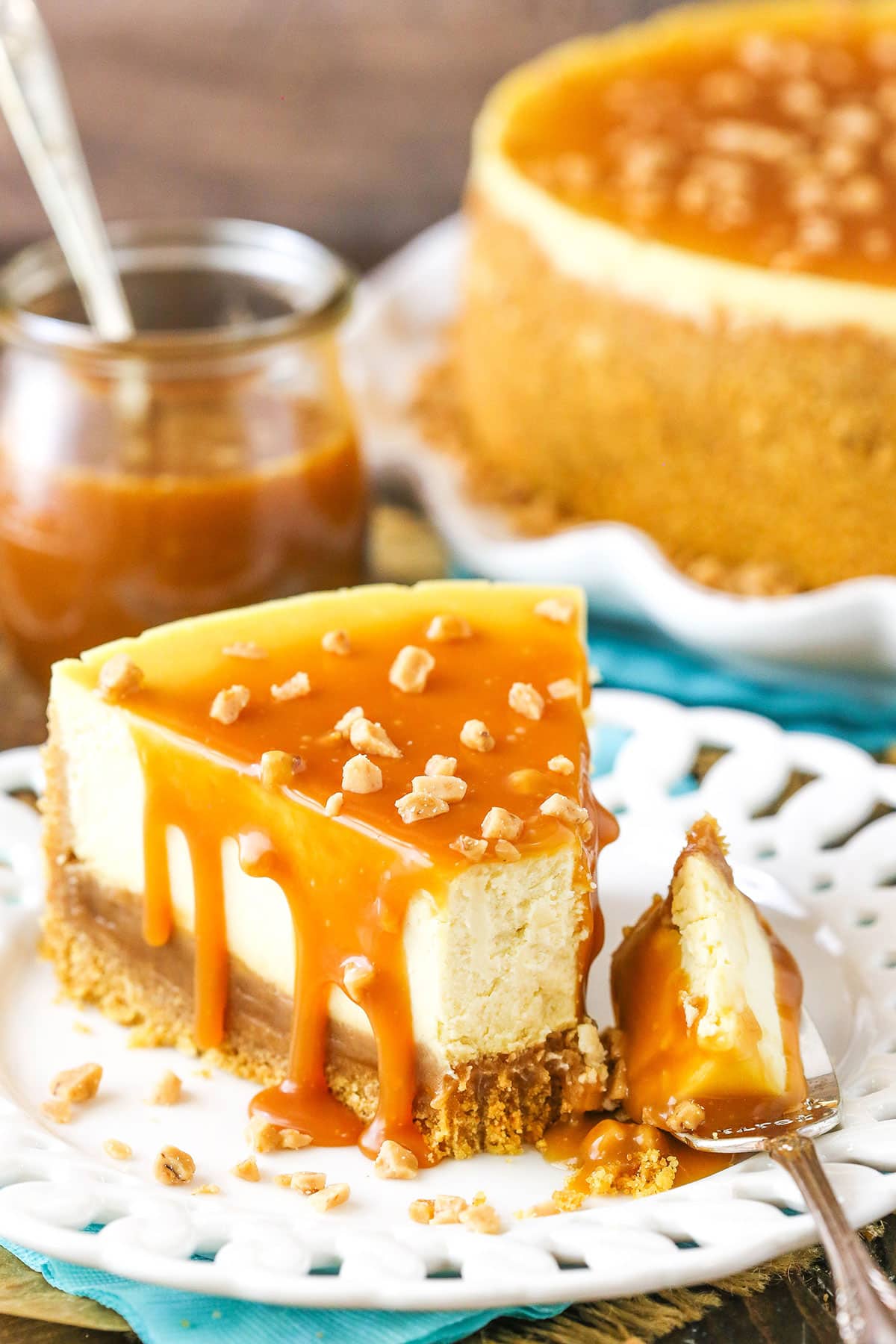 A slice of Salted Caramel Cheesecake with a bite removed next to a fork on a white plate