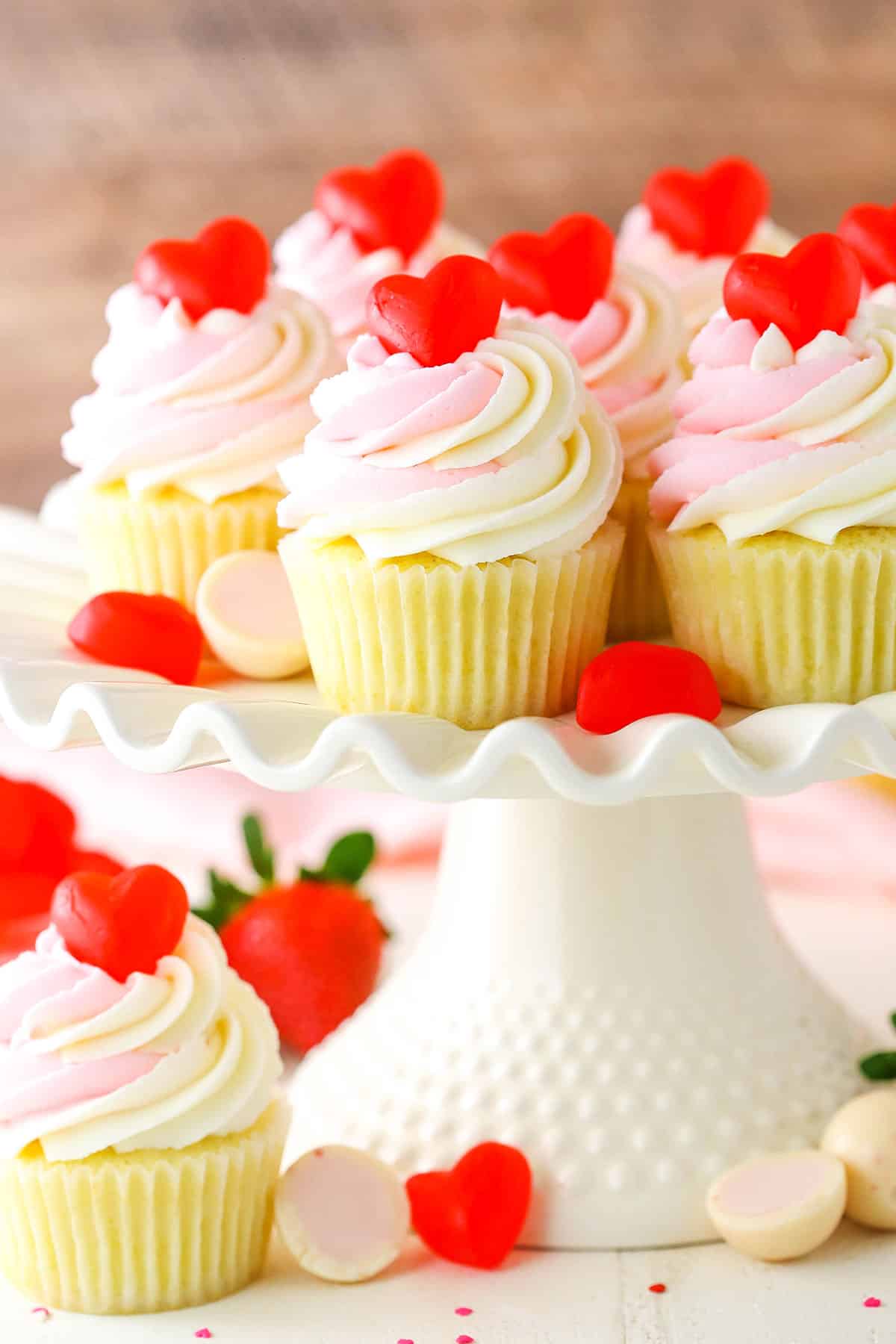 These Strawberry Truffle Cupcakes are moist vanilla cupcakes filled with strawberry truffle filling, topped with white chocolate buttercream! Strawberry Truffle Cupcakes on a white cake stand