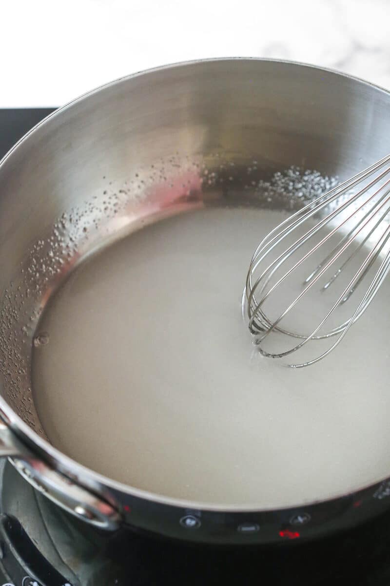 Metal pot with whisk mixing sugar and water.