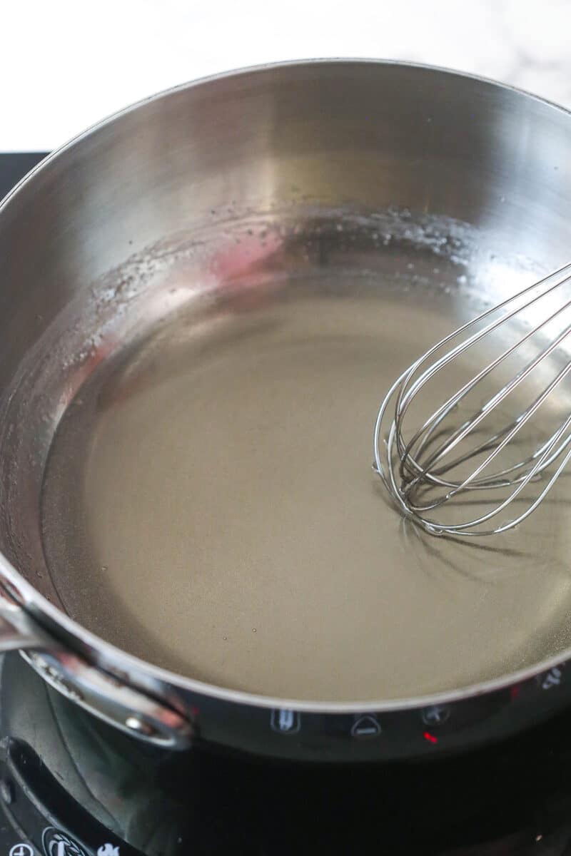 Metal pot with whisk mixing fully dissolved sugar and water.