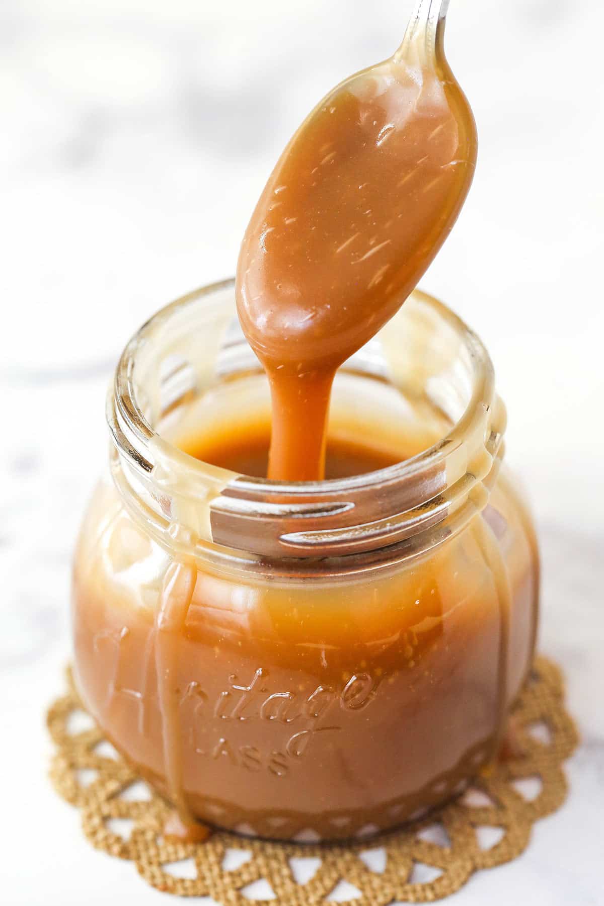 Spoon covered in thick coating of Bourbon Caramel Sauce dripping into a jar.