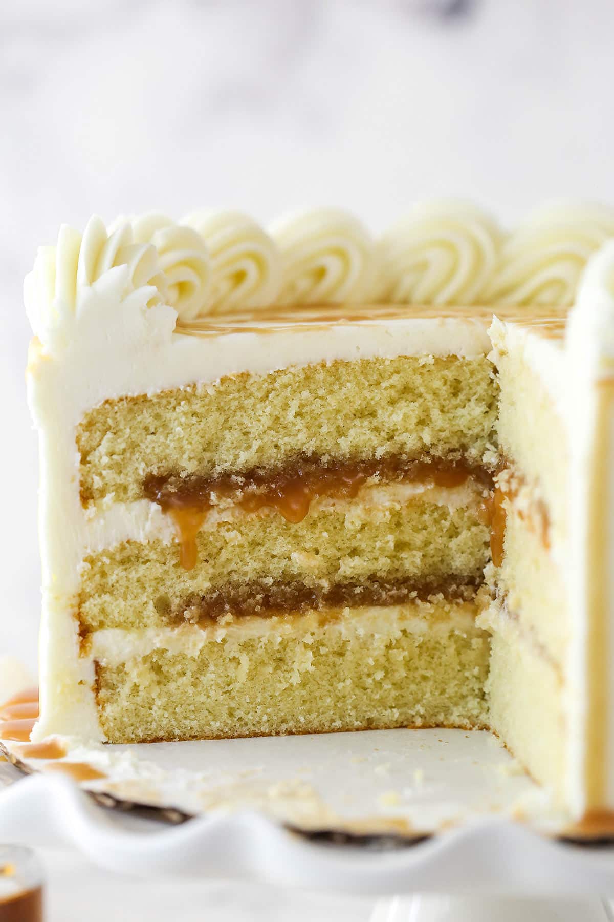 Bourbon cake is made of 3 layers of moist, bourbon-infused vanilla cake layered with vanilla-bourbon buttercream & bourbon caramel sauce. Bourbon cake with a couple of slices taken out of it.