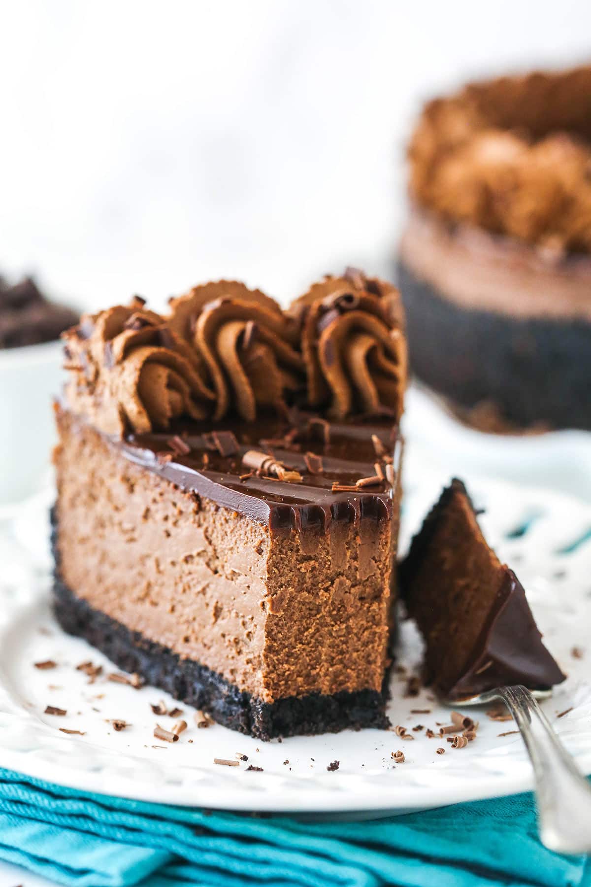 A slice of chocolate cheesecake on a plate with a fork taking a bit out of it.