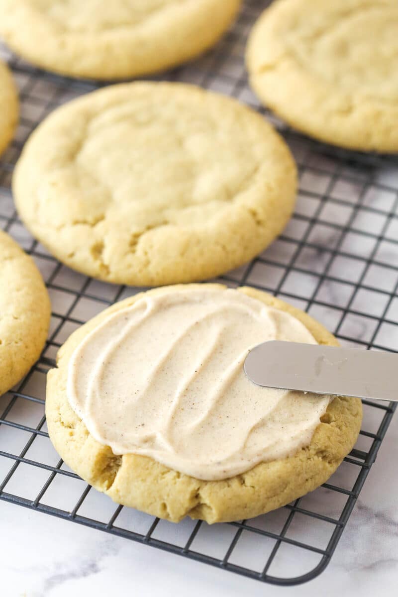 A knife spreading frosting on a copycat Crumbl apple crumb cake cookie.