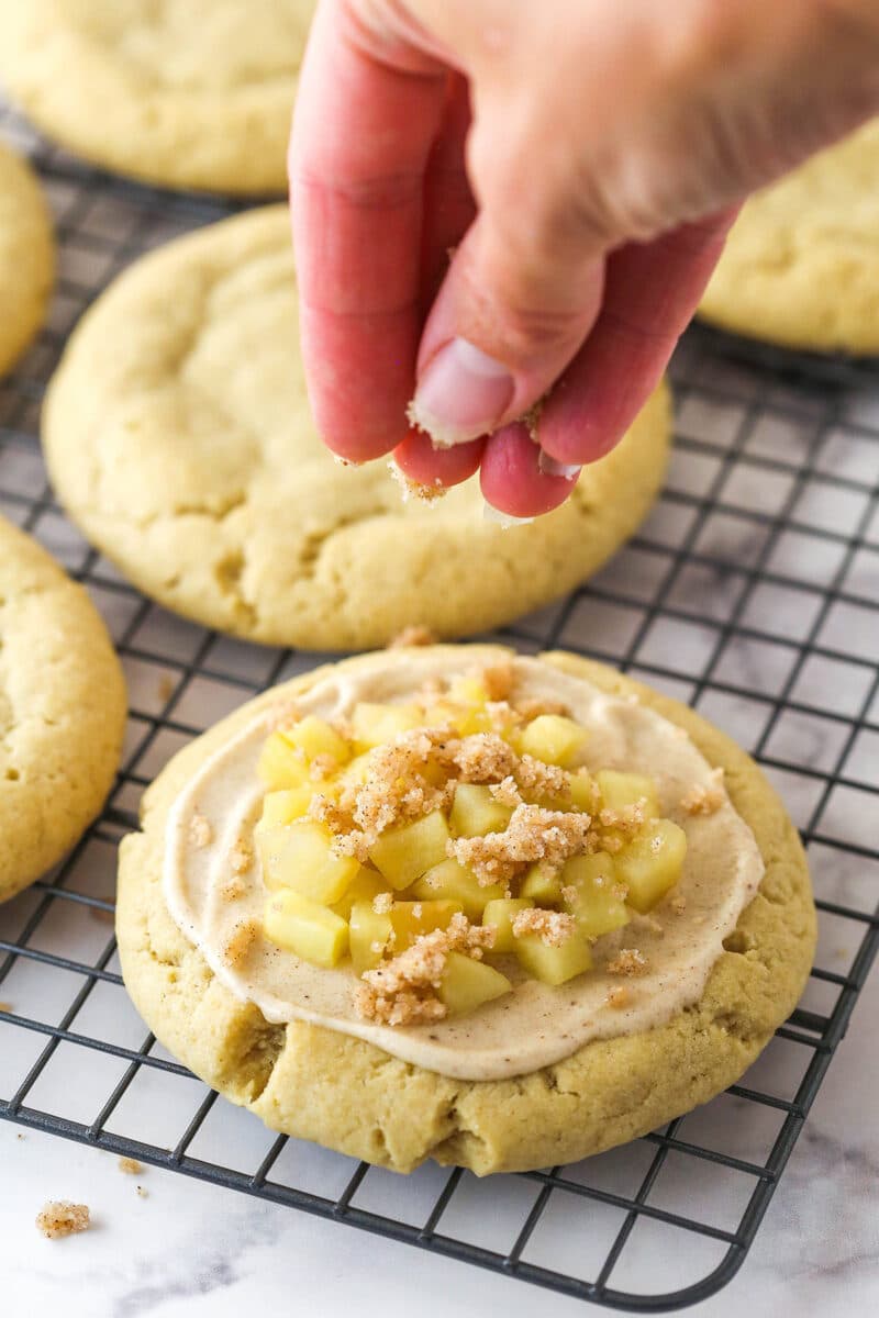 A hand sprinkling the streusel topping over an apple crumb cookie.