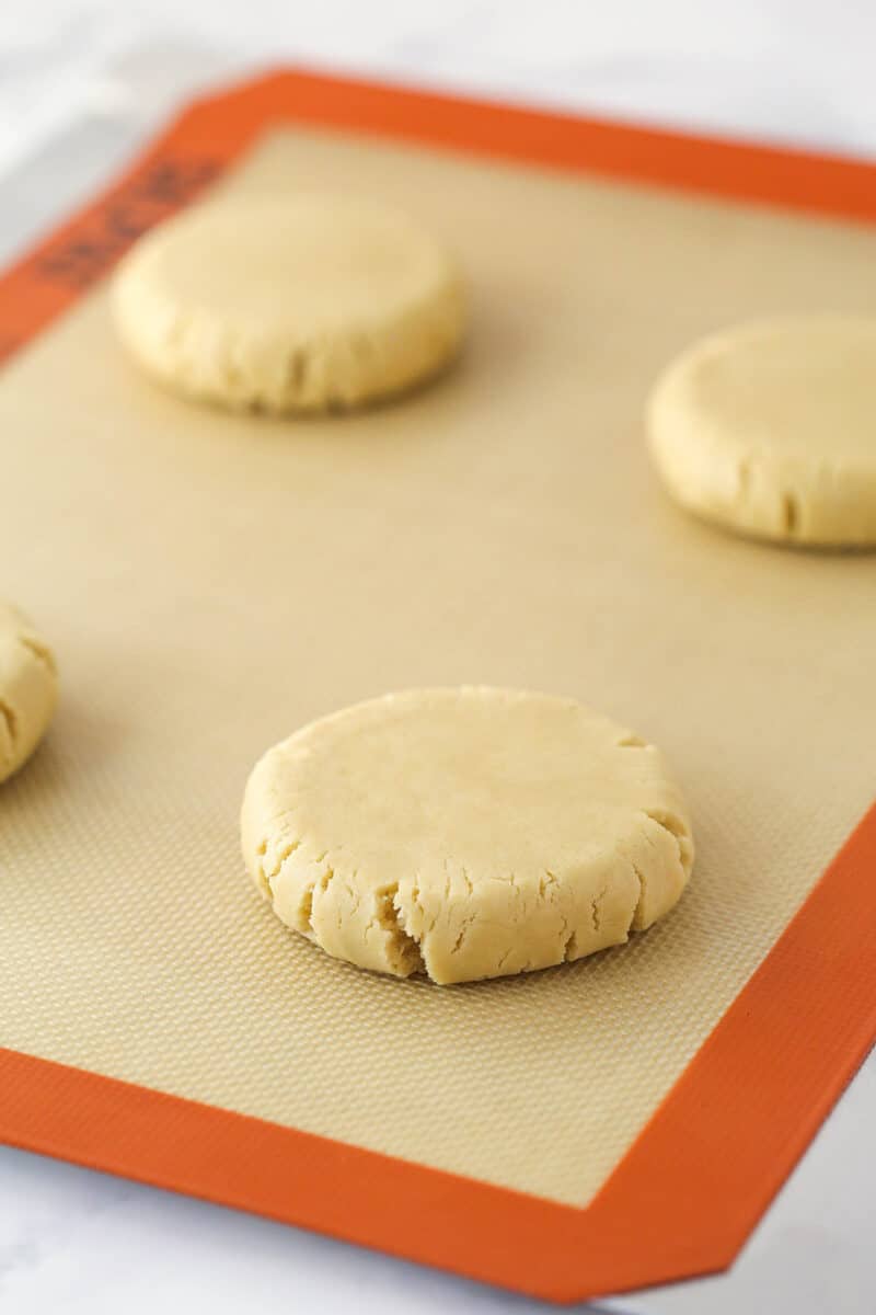 4 flattened apple crumble cookie balls on a baking mat.