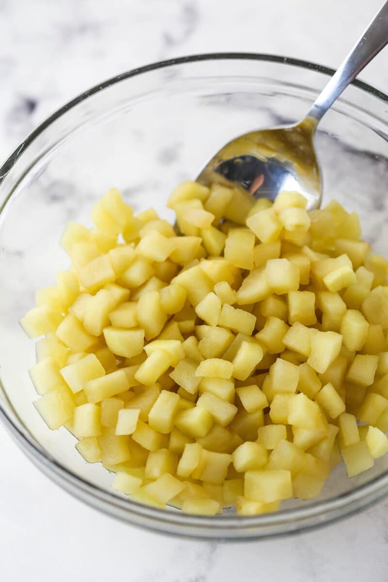 A spoon in a clear bowl of finely chopped, cooked apples.