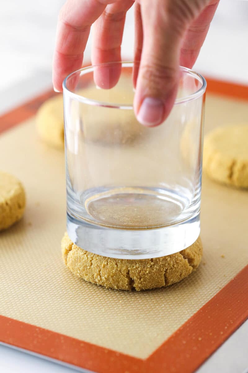Using the bottom of a glass to press graham cracker cookies flat on a silicon baking mat.