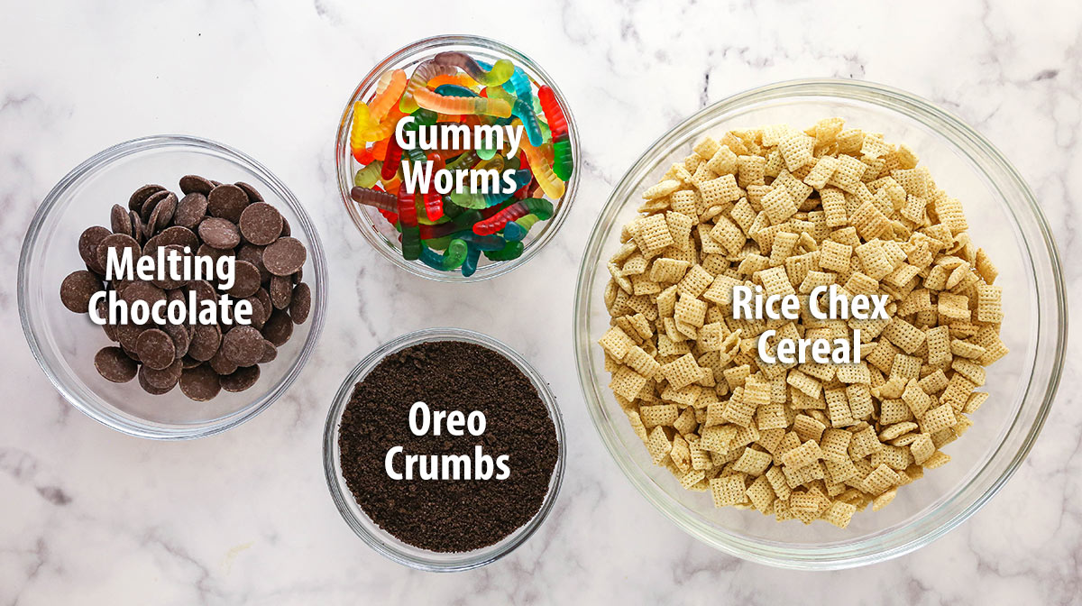 Marble surface holding bowls of the ingredients needed to make Dirt and Worms Puppy Chow with text labels.