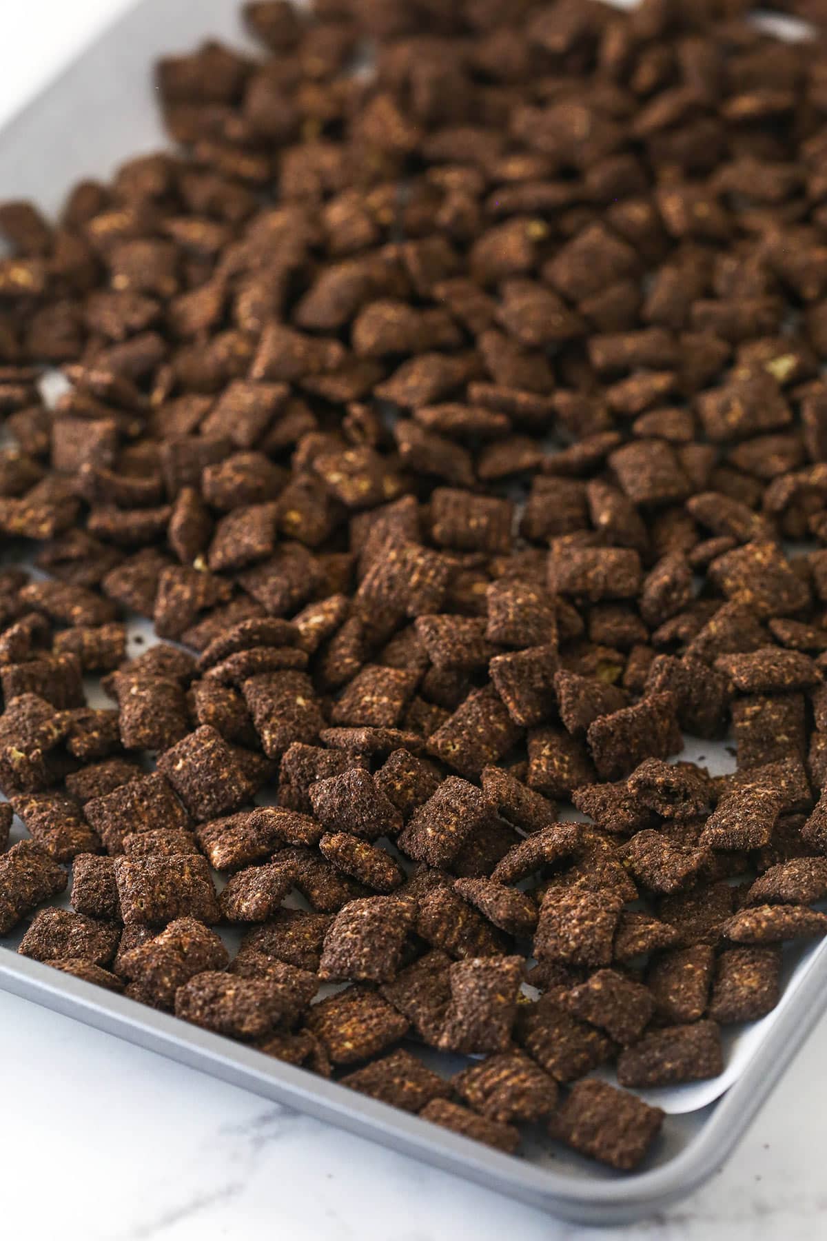 Chocolate covered Chex cereal laid out on a parchment paper-lined baking sheet for Dirt and Worms Puppy Chow.