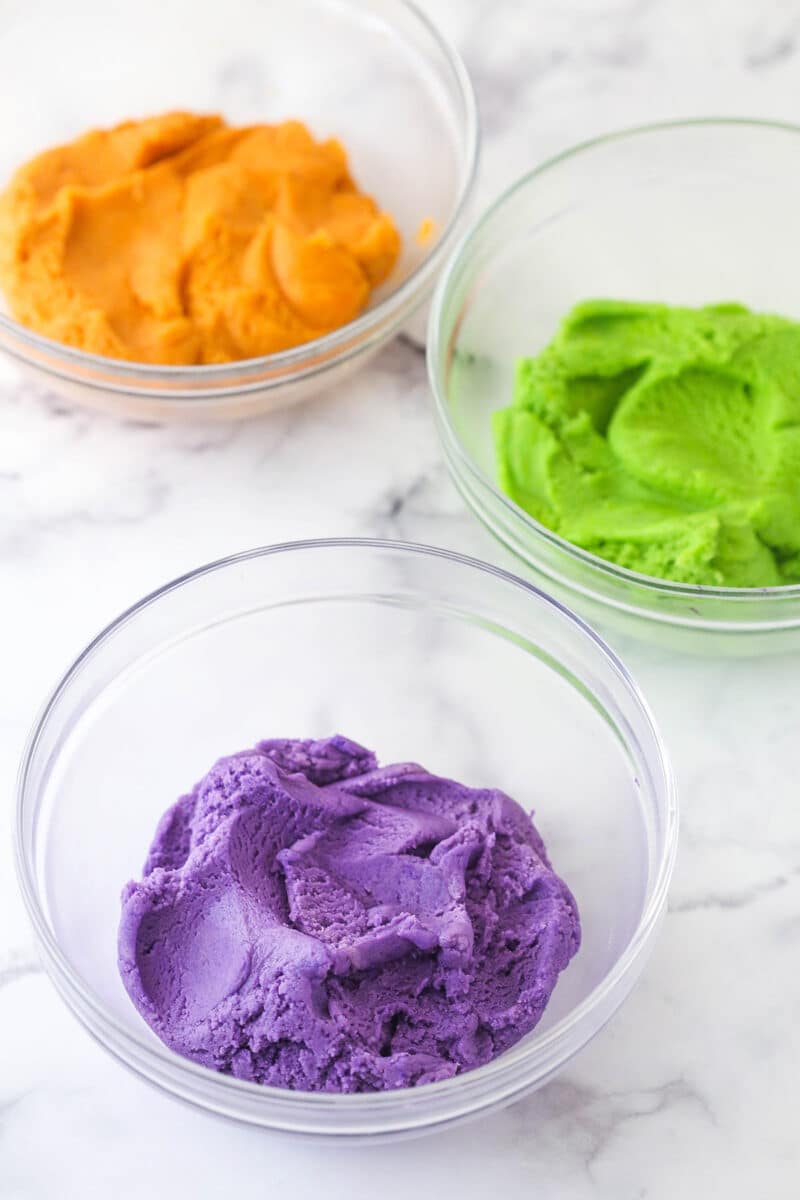 3 small glass bowls of dyed cookie dough for Halloween Monster Cookies.