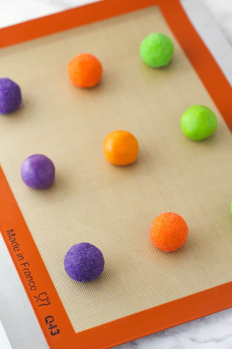 A silicon baking mat covered in colorful cookie dough balls for Halloween Monster Cookies.