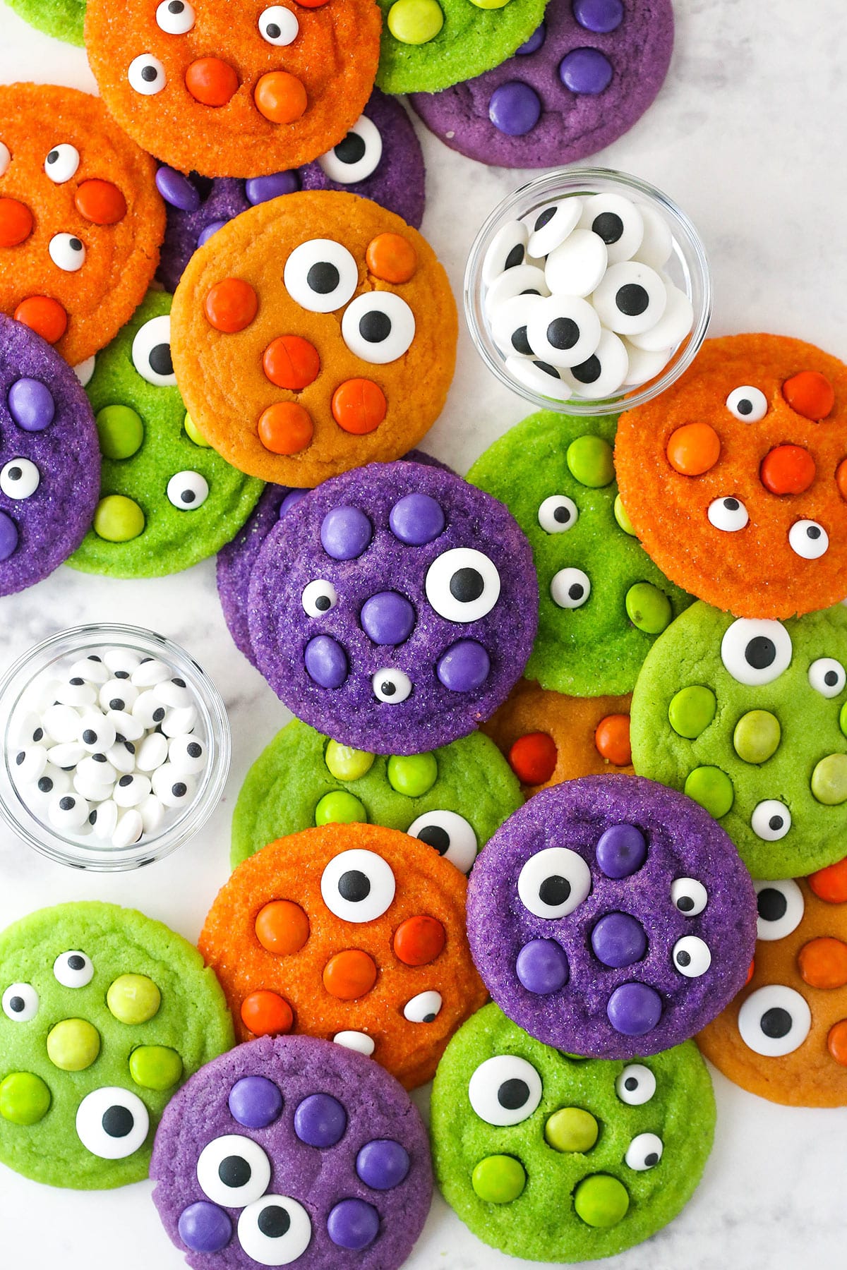Top view of a pile of brightly colored Halloween Monster Cookies on marble table with eyeballs.