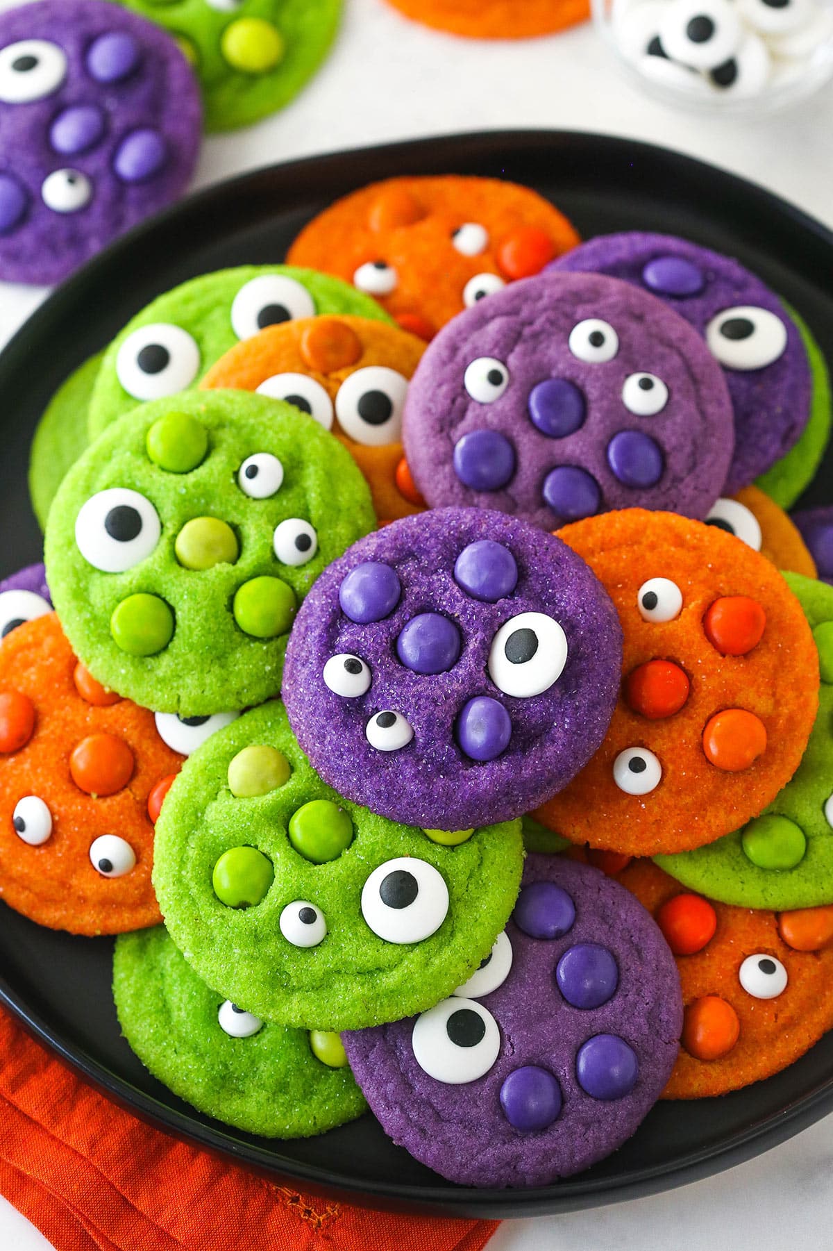 A pile of brightly colored Halloween Monster Cookies on a black plate.