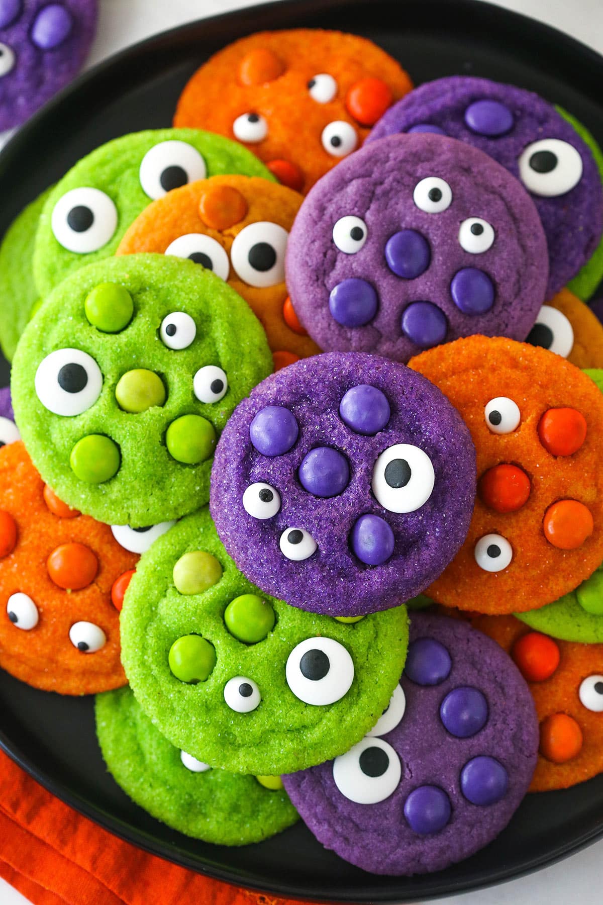 Close up of a pile of brightly colored Halloween Monster Cookies on a black plate.