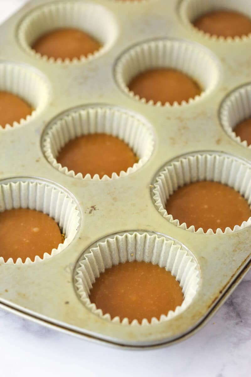 Caramel sauce spooned over graham cracker crust in cupcake liners in a cupcake pan.