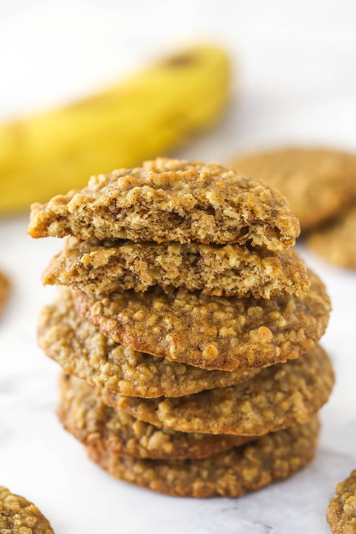 A stack of Moist and Chewy Banana Oatmeal Cookies with the top cookie broken in half to show texture.