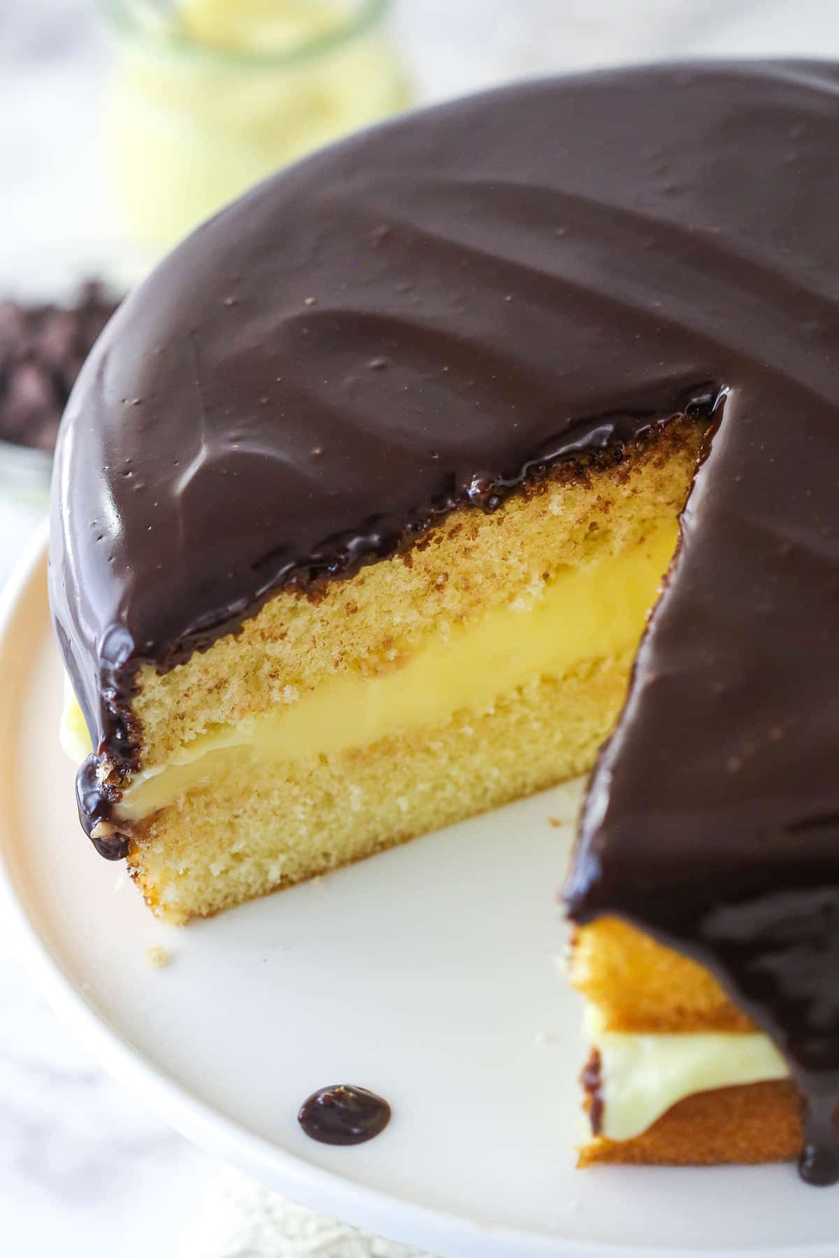 Overhead image of Boston cream pie on a cake stand with a slice taken out of it.