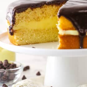 Boston cream pie on a cake stand with a slice taken out of it.