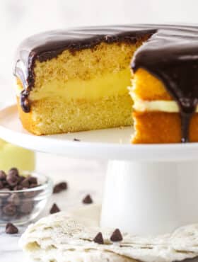 Boston cream pie on a cake stand with a slice taken out of it.
