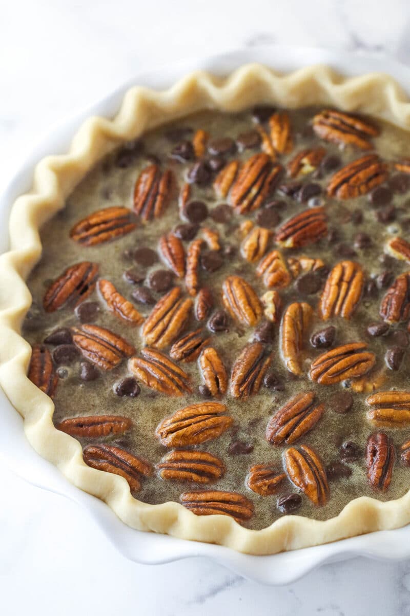 Chocolate pecan pie recipe features a luscious, buttery filling loaded with pecans & chocolate chips. A wonderful spin on the classic. Chocolate pecan pie filling in a pie crust ready to be baked.