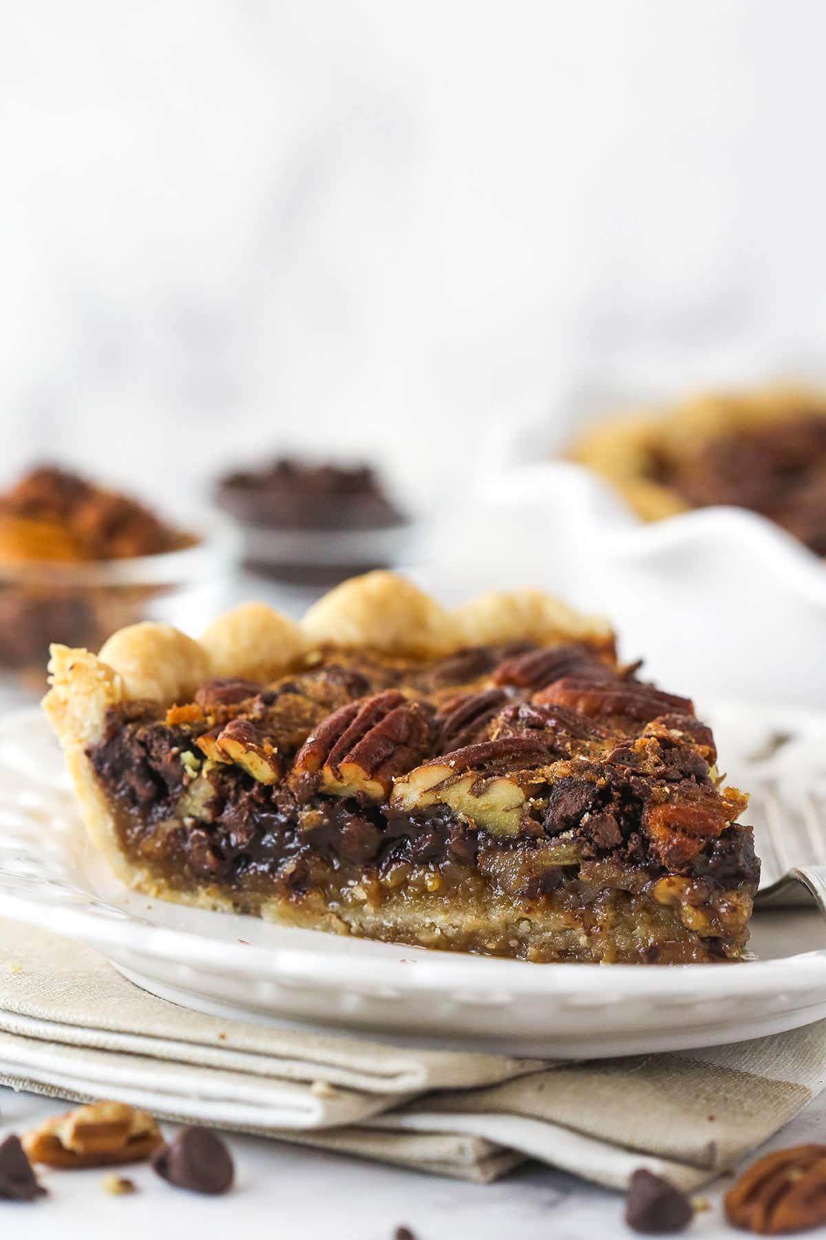 Side view of a slice of chocolate pecan pie on a plate with a fork.