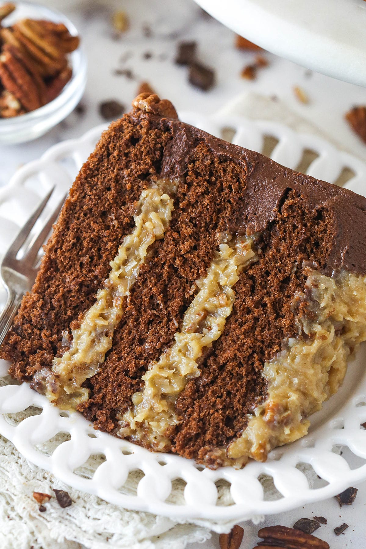 This classic German chocolate cake is made of moist layers of chocolate cake, coconut pecan filling, and chocolate buttercream. A slice of german chocolate cake on a plate with a fork.