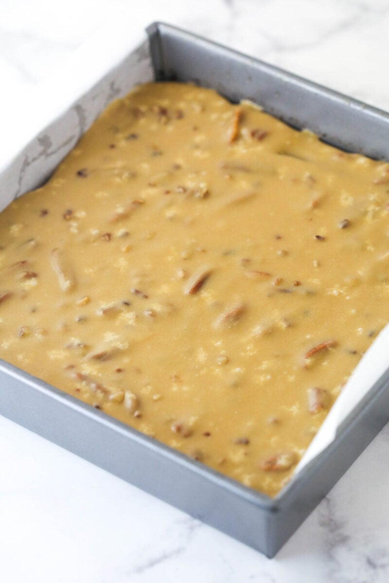 Praline frosting spread over the top of baked brownies in a metal baking pan.