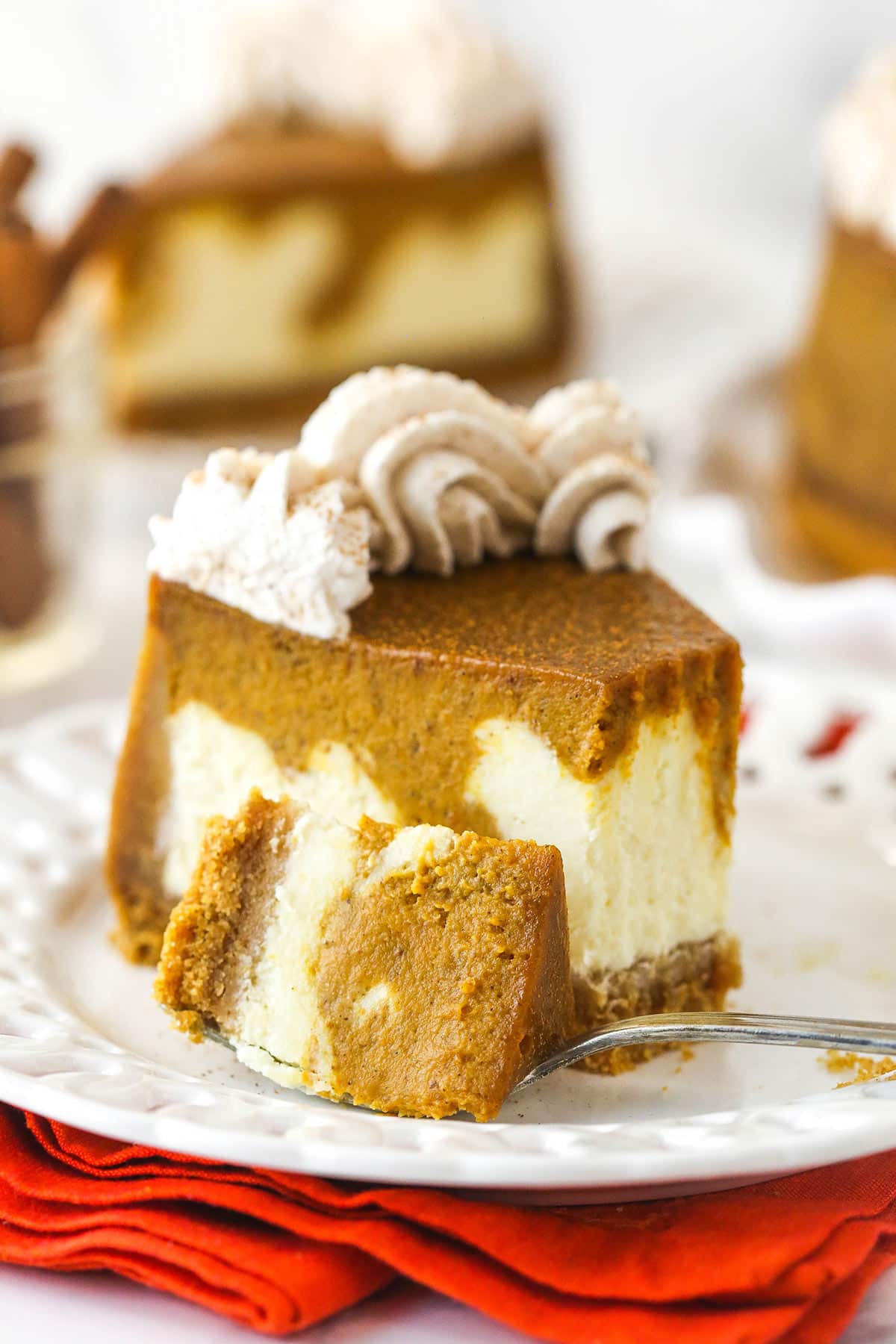 A fork taking a bite out of of a slice of pumpkin cheesecake on a plate.